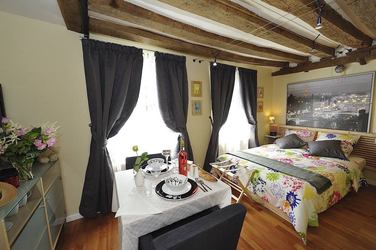 A cozy room with a bed, a dining table set for two, and a window with curtains.