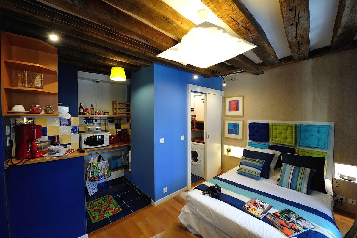 A compact bedroom with a bed, a washing machine, and a kitchenette.