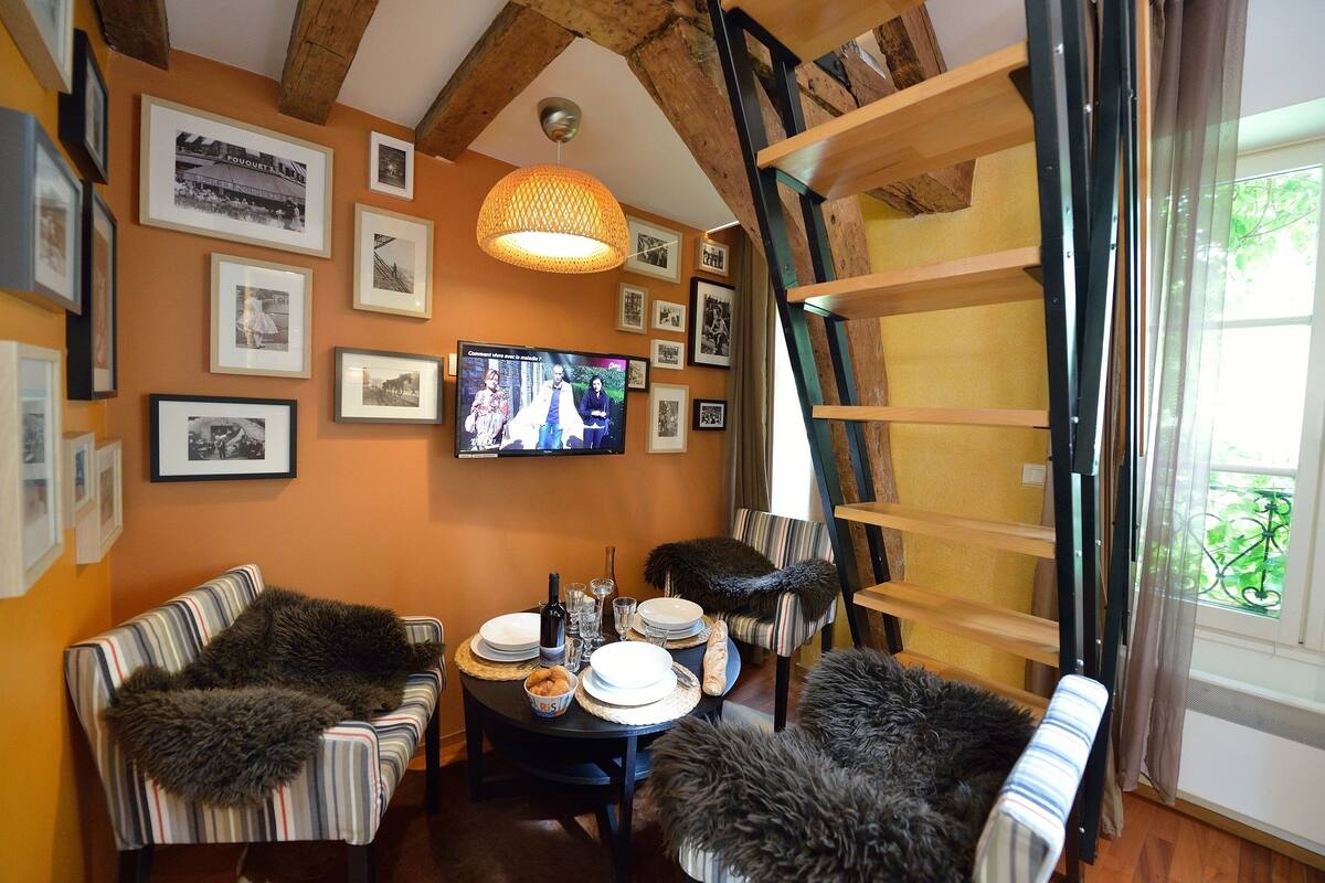 A cozy room with a dining table set for four, surrounded by striped sofas and a television displaying a program.