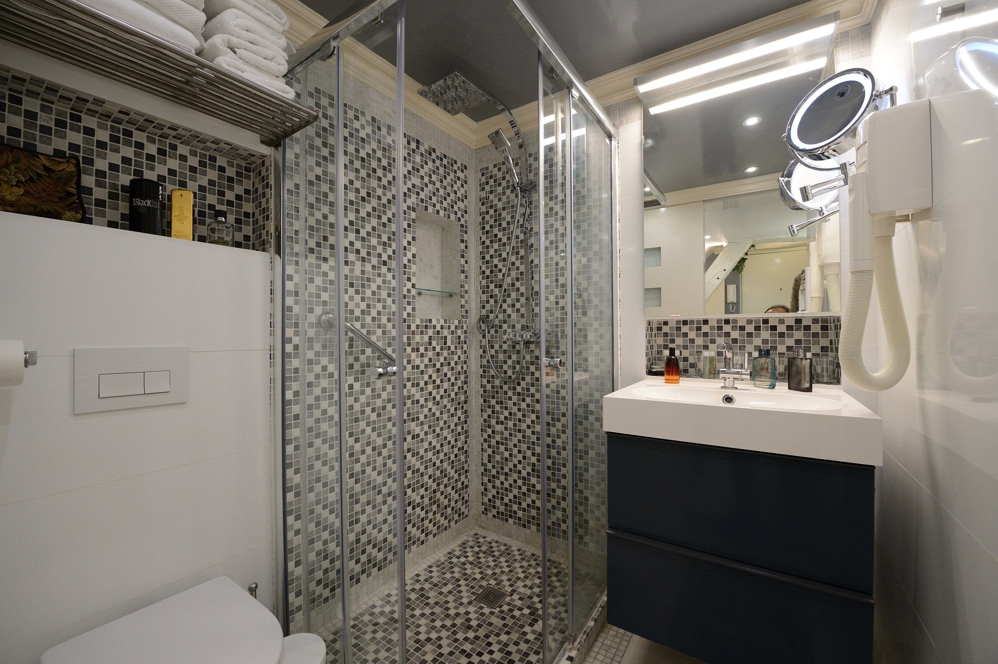 A modern bathroom with a glass-enclosed shower, a white sink with a mirror, and a tiled floor.