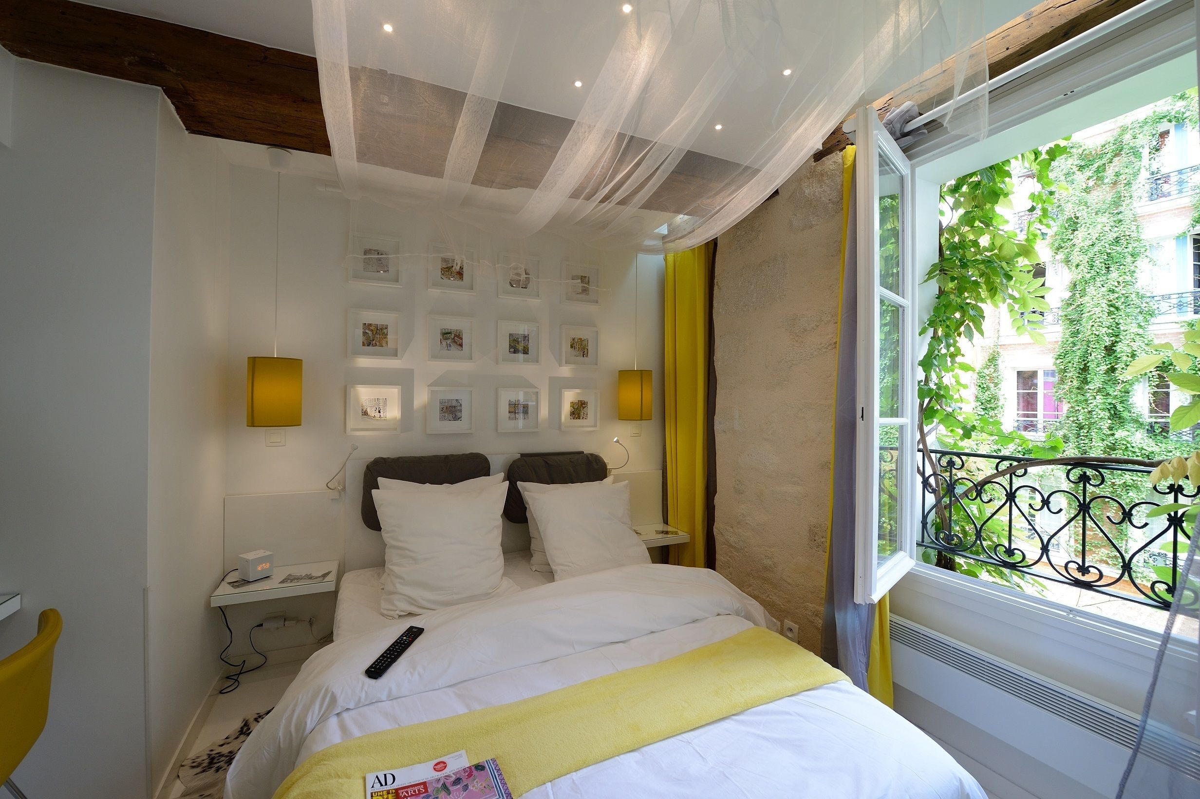 A hotel room with a bed, bedside tables, a window with a view of greenery, and wall-mounted picture frames.