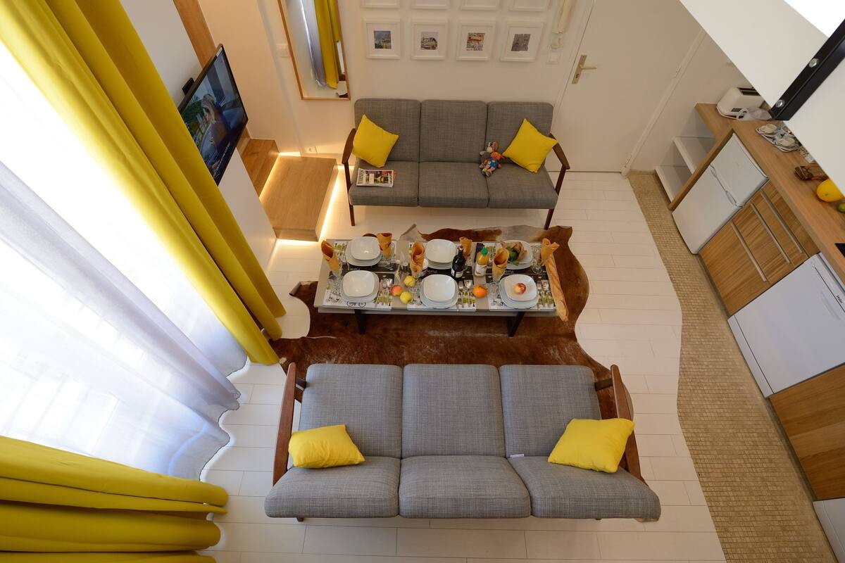 A modern living room with a grey sofa and a dining table set for four.
