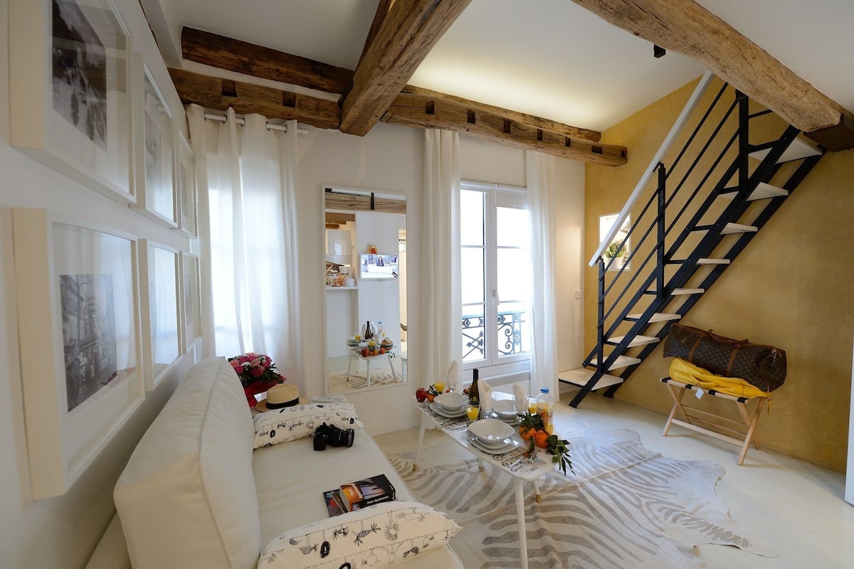 A spacious living room with a high ceiling, a staircase, and a balcony.