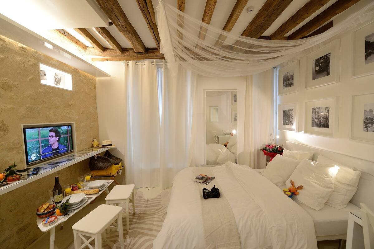 A hotel room with a bed, a desk with a television, a mirror, and framed pictures on the wall.
