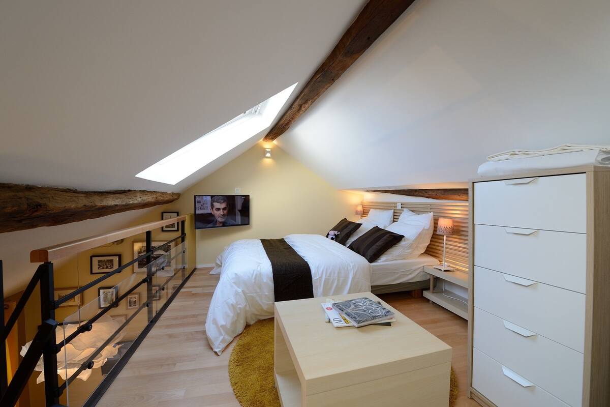 A bedroom with a sloped ceiling, a bed with white bedding, a bedside table with a lamp, and a wardrobe.