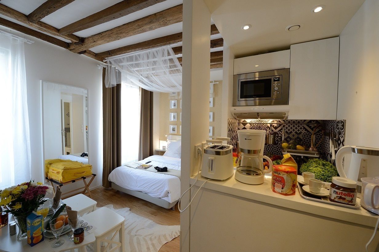 A hotel room with a bed, a small kitchenette with a microwave, coffee maker, and breakfast items, and a suitcase on a trolley.