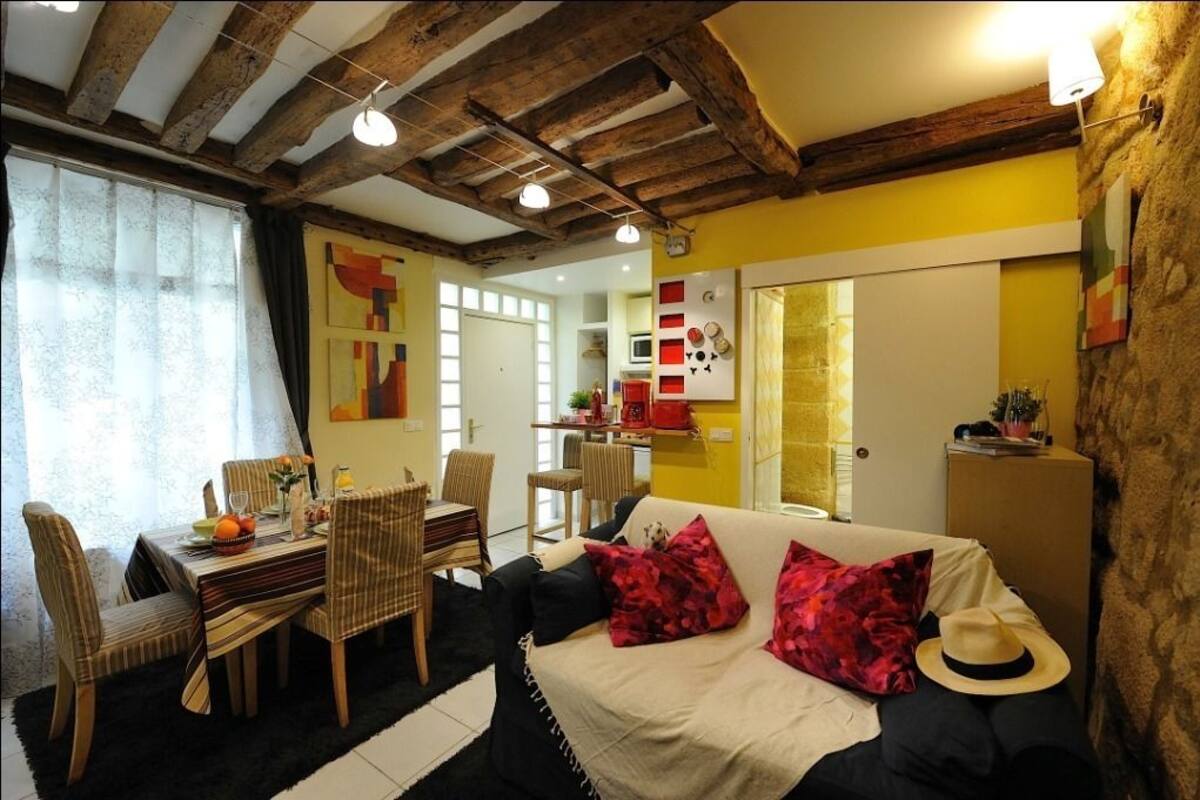 A cozy living room with a dining area, wooden beams on the ceiling, and a yellow accent wall.