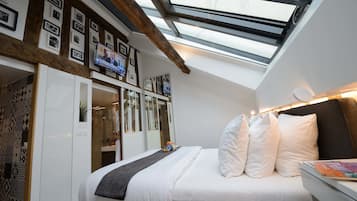 A bedroom with a skylight, a bed with white bedding, a bedside table, and a TV mounted on the wall.
