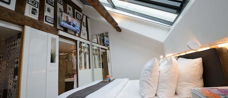 Ein Schlafzimmer mit Dachfenster, einem Bett mit weißer Bettwäsche, einem Nachttisch und einem an der Wand montierten Fernseher.