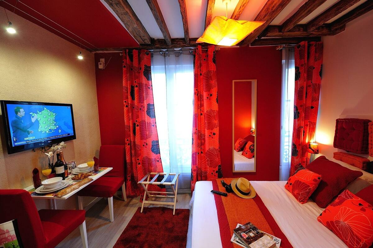 A hotel room with a bed, a desk with breakfast items, a TV, and red curtains.