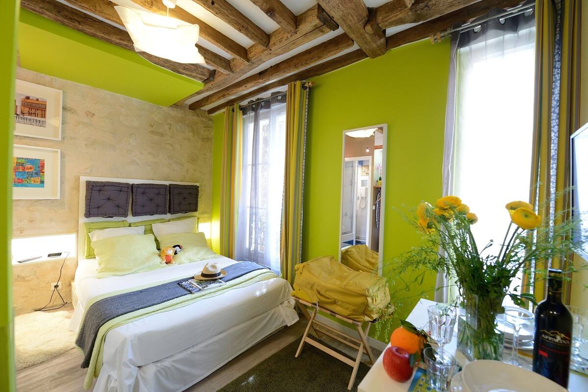 A room with a bed, a table with a vase of flowers, and a window with curtains.