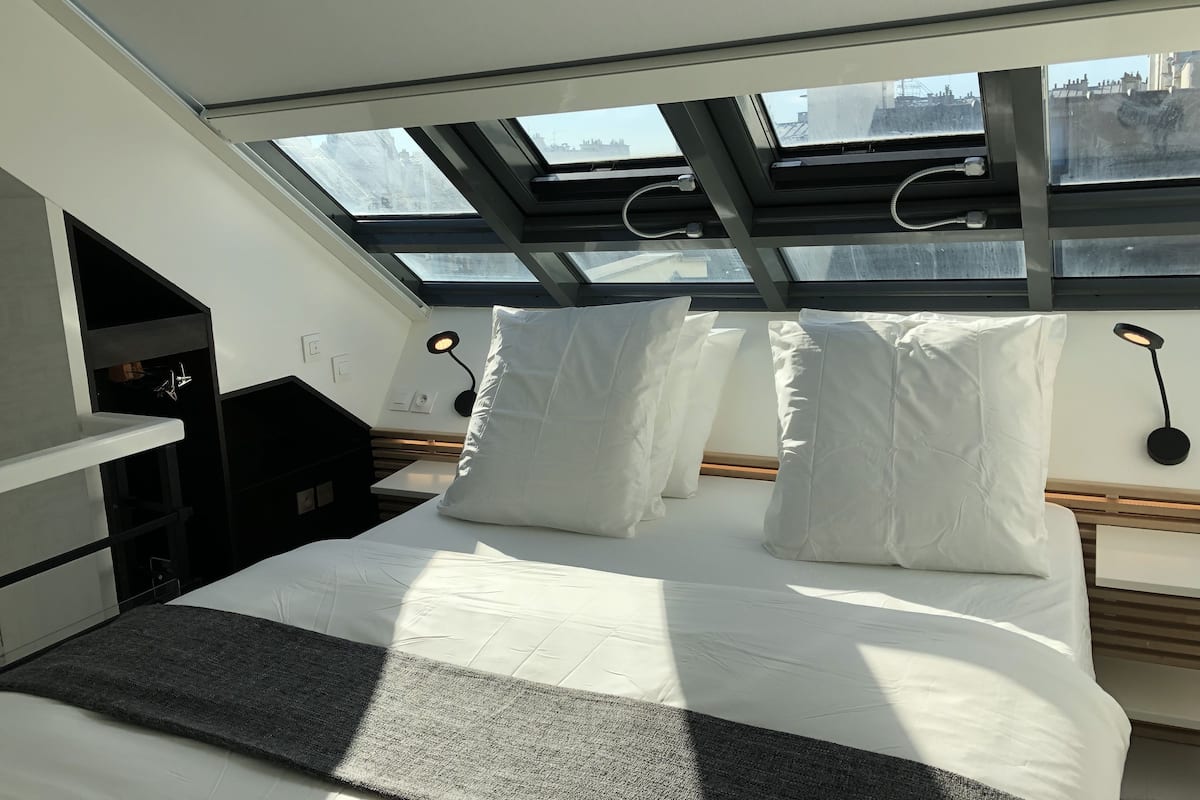 A modern bedroom with a skylight, a bed with white linens, a bedside table, and a black lamp.
