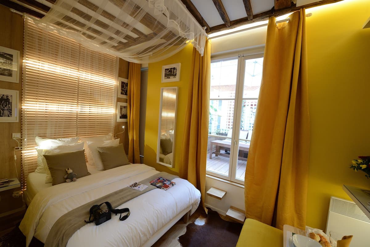 A hotel room with a bed, a bedside table, a window with curtains, and a view of the outside.