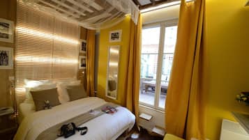 A hotel room with a bed, a bedside table, a window with curtains, and a view of the outside.