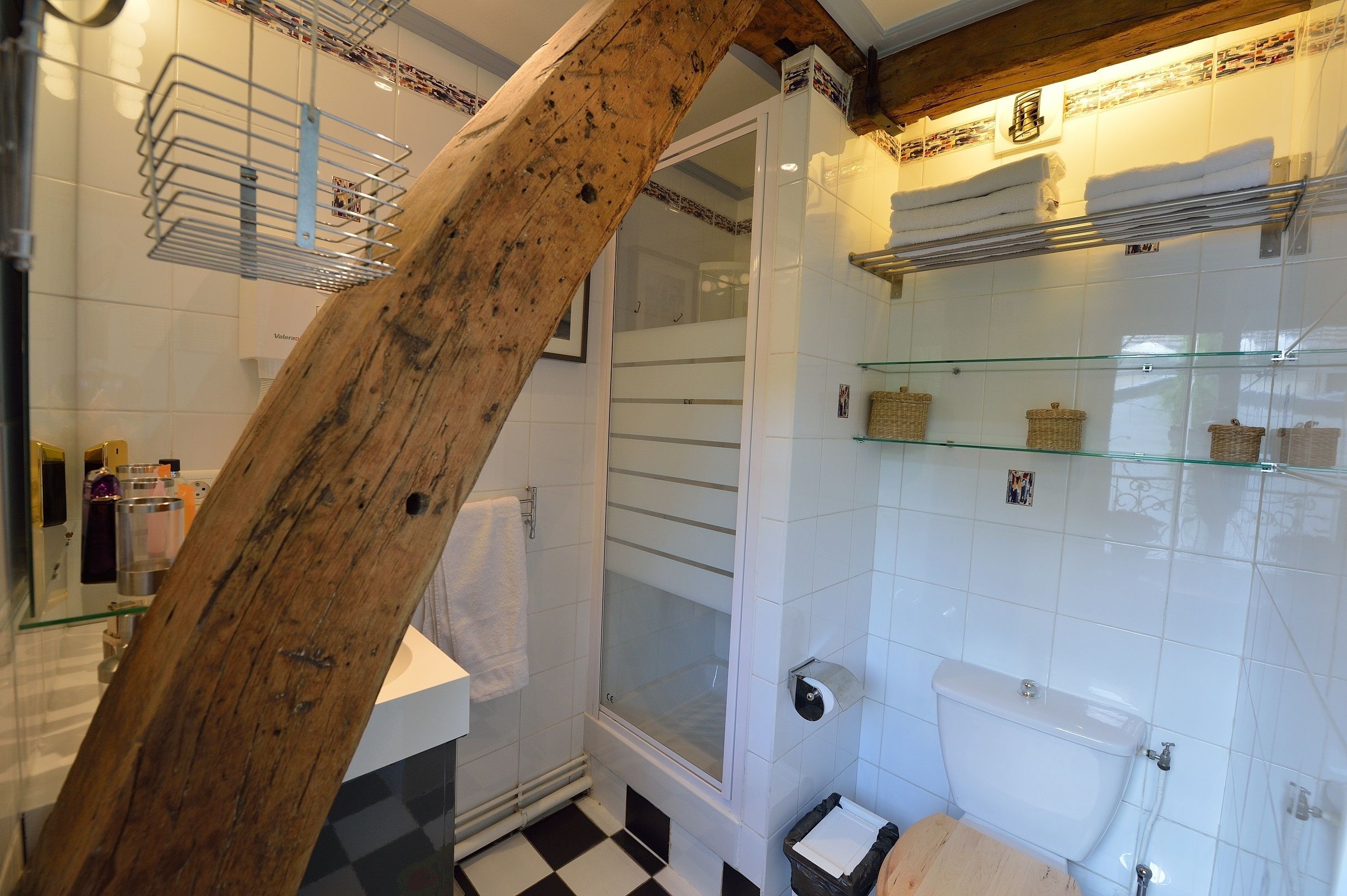 Een badkamer met een houten balk, een glazen douchecabine, een toilet en een wastafel.