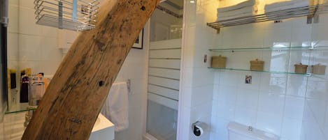 Een badkamer met een houten balk, een glazen douchecabine, een toilet en een wastafel.