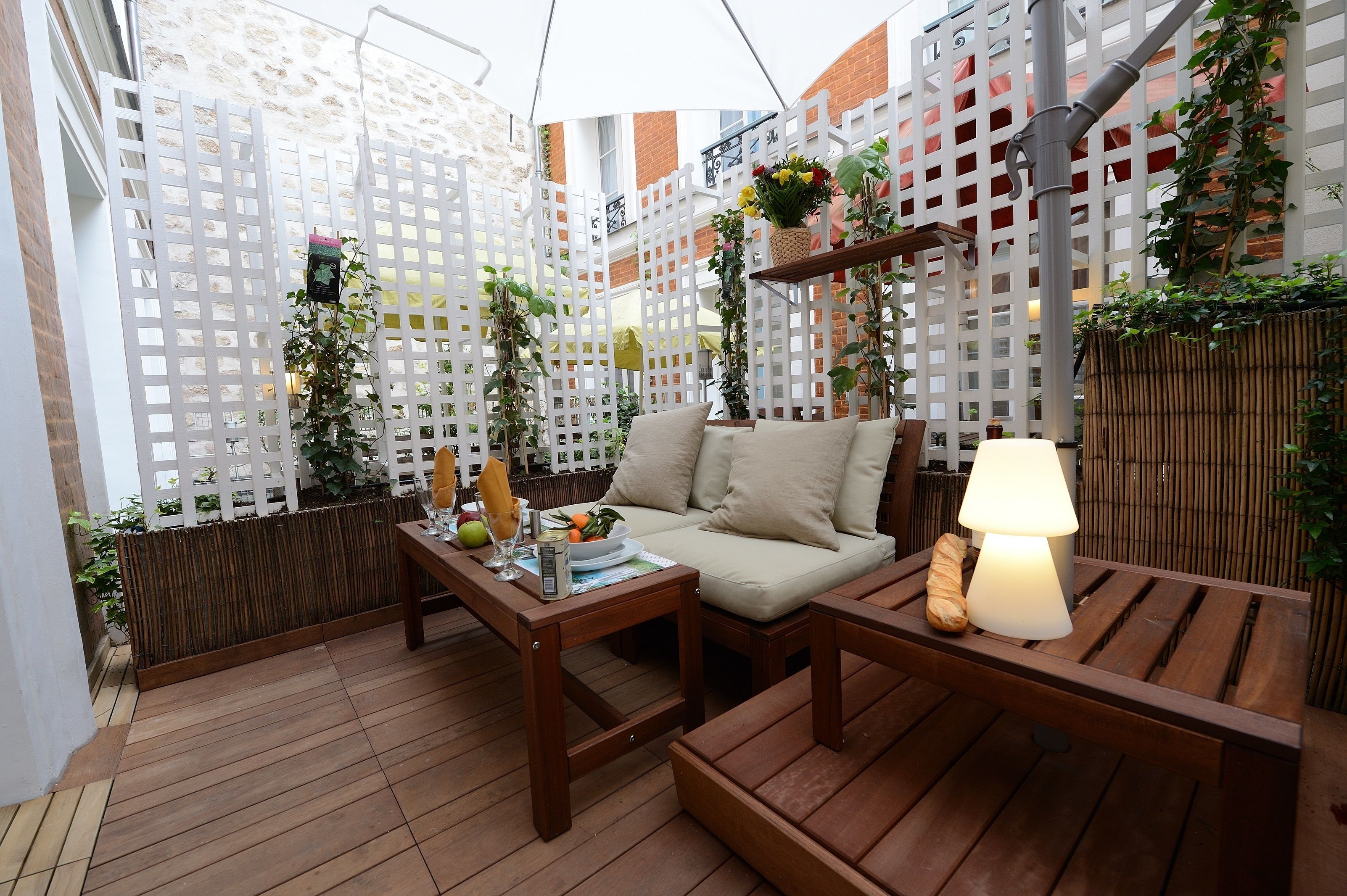 Un espace extérieur accueillant, aménagé avec du mobilier en bois, une table avec une lampe et une clôture blanche en treillis.