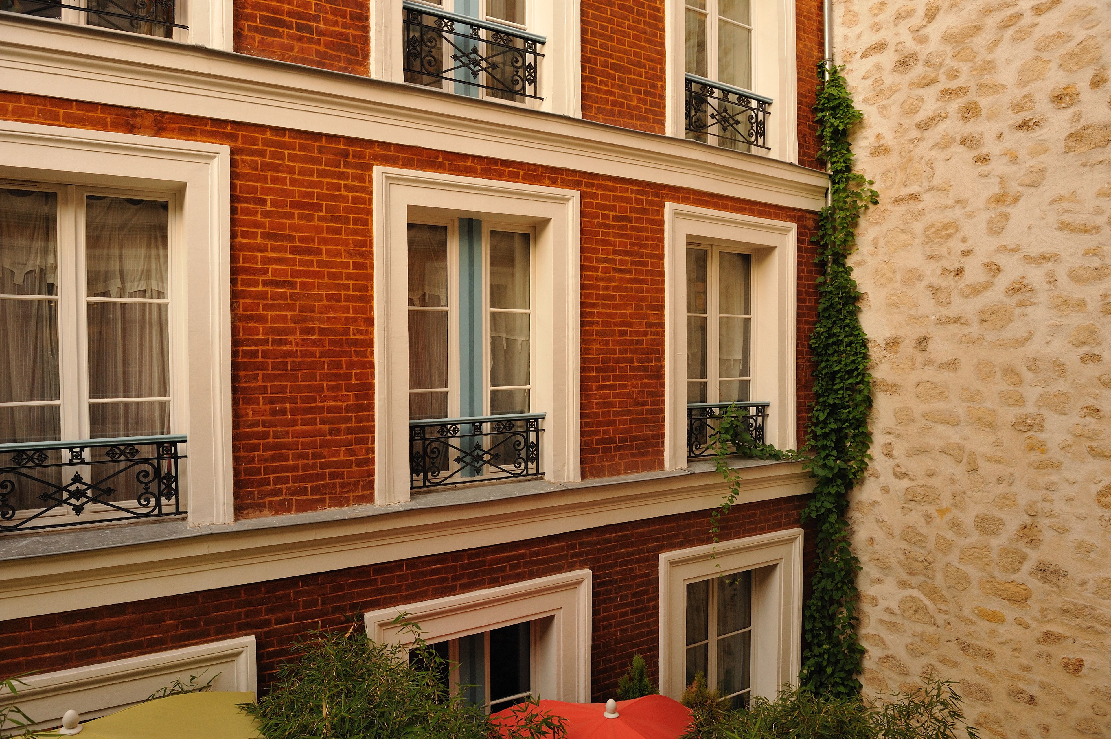 Un edificio de varios pisos con paredes de ladrillo rojo, marcos de ventanas blancos y balcones de hierro forjado negro.