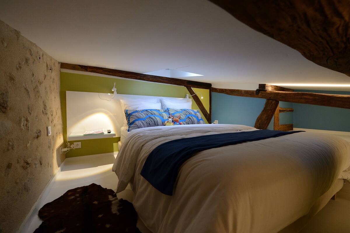 A bedroom with a bed, a bedside table, a lamp, and a window.