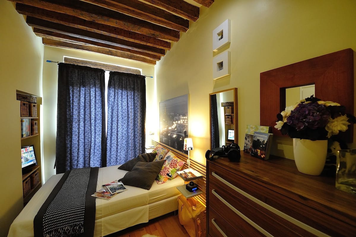 A hotel room with a bed, a nightstand, a mirror, a dresser, and a window with curtains.