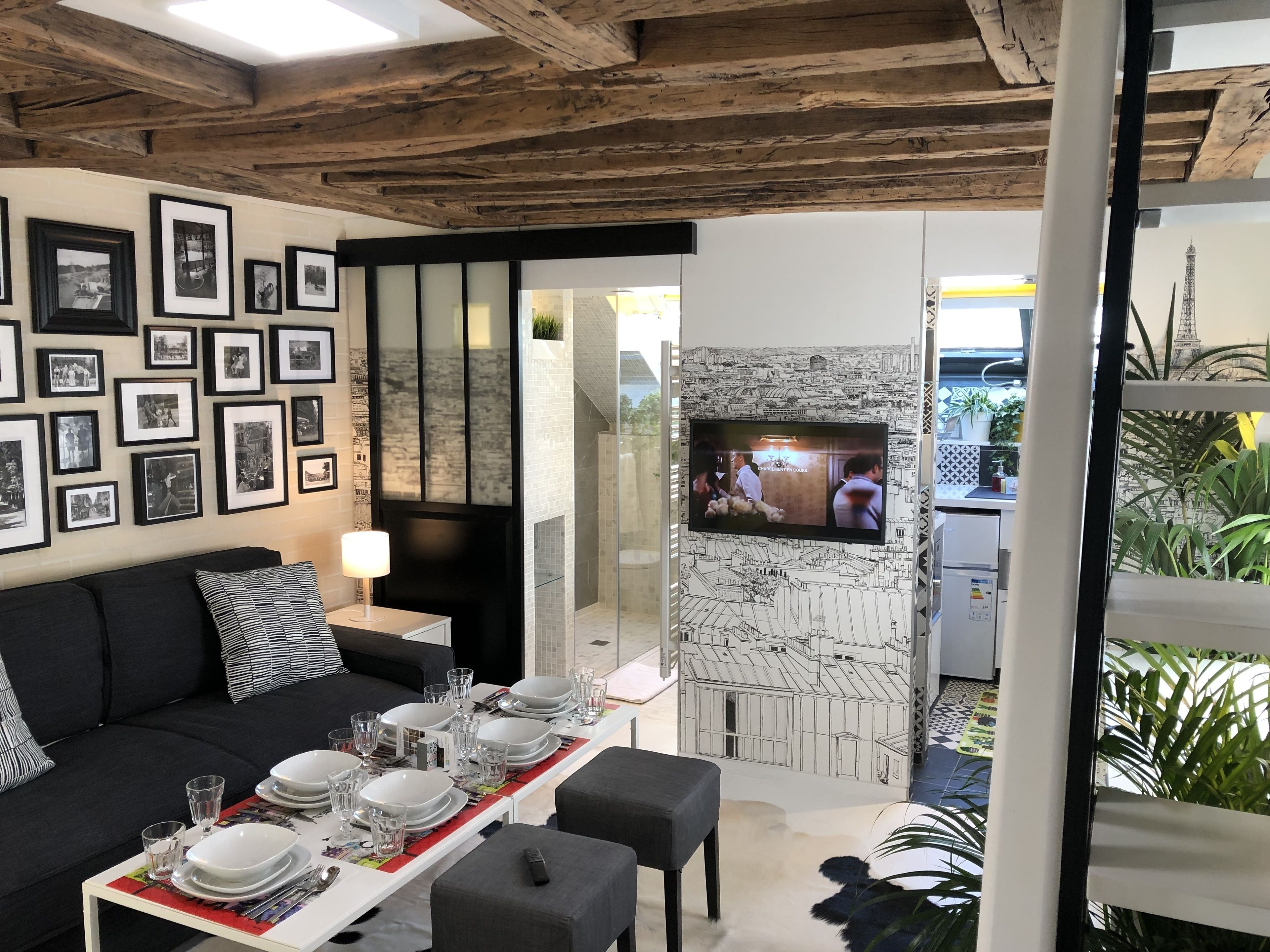 A dining area with a table set for four, a black sofa, and framed pictures on the wall.