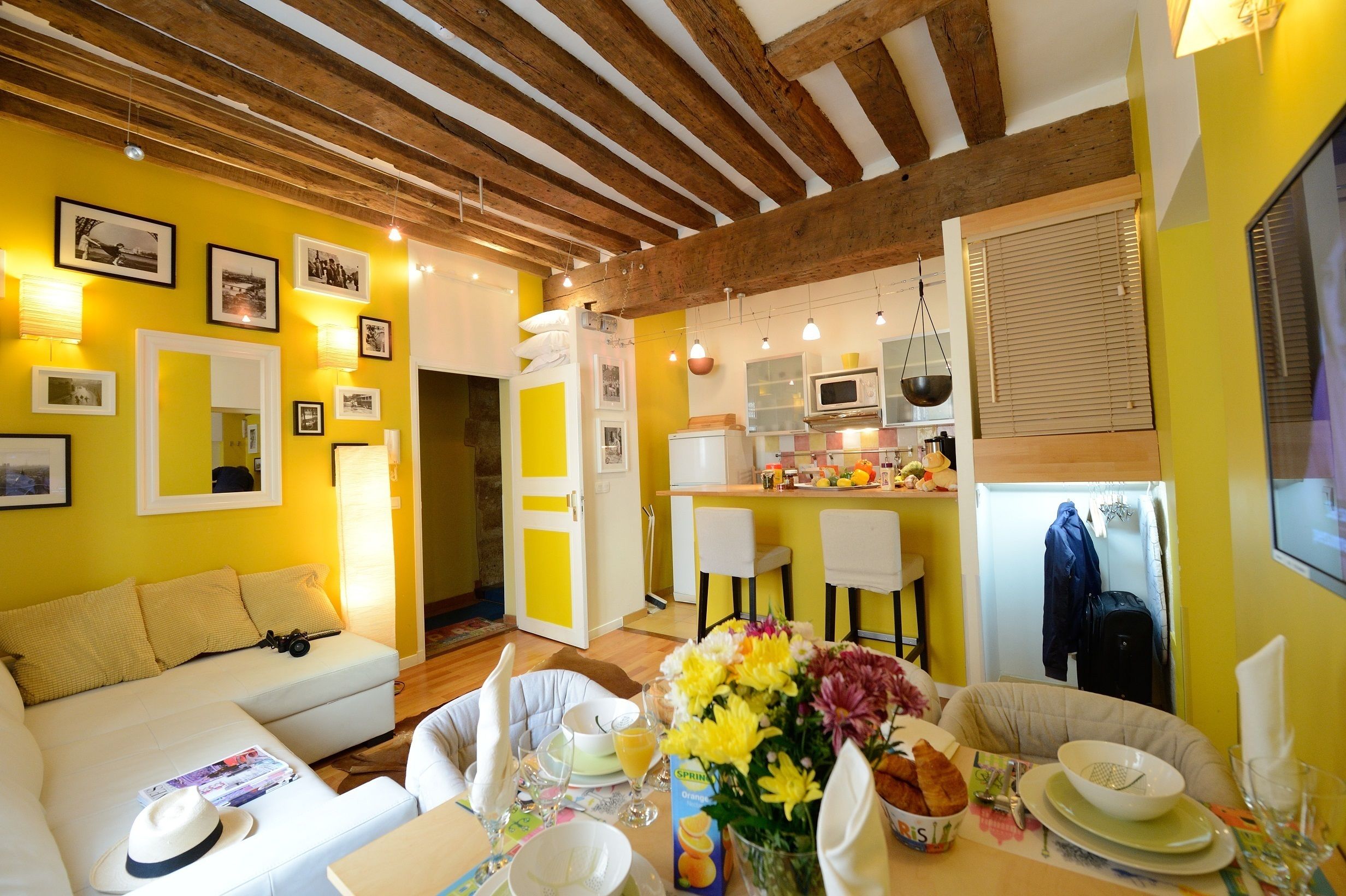 A cozy living room with a sofa, dining table set with flowers, and a kitchen in the background.
