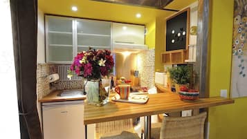 Une cuisine compacte avec un plan de travail en bois, un petit réfrigérateur, une fenêtre et un vase de fleurs.