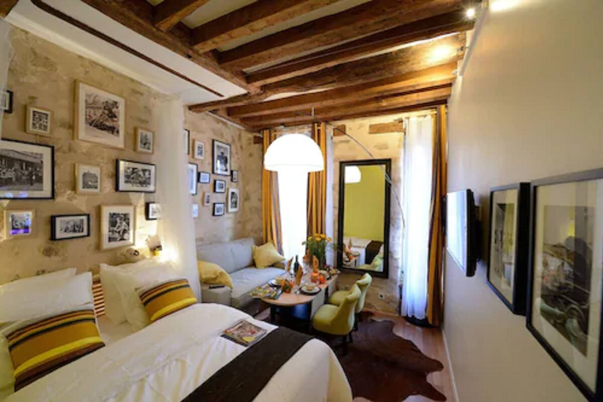 A cozy bedroom with a bed, a sofa, a dining table with chairs, and framed pictures on the walls.