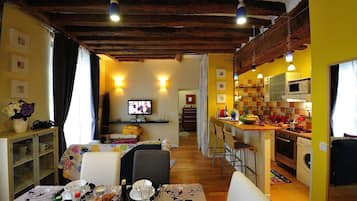 A cozy kitchen with a wooden ceiling, a dining area with a table set for two, and a television in the background.