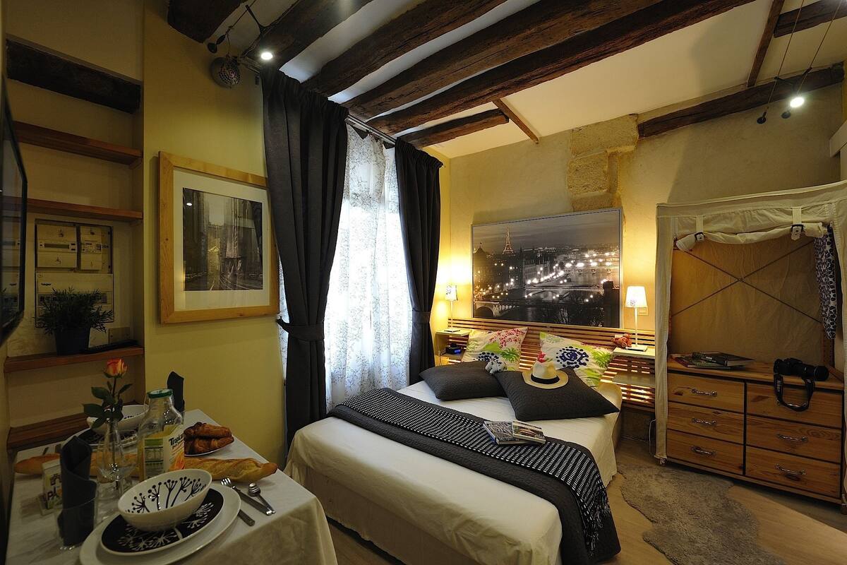 A hotel room with a bed, bedside table, lamp, and a cityscape view.