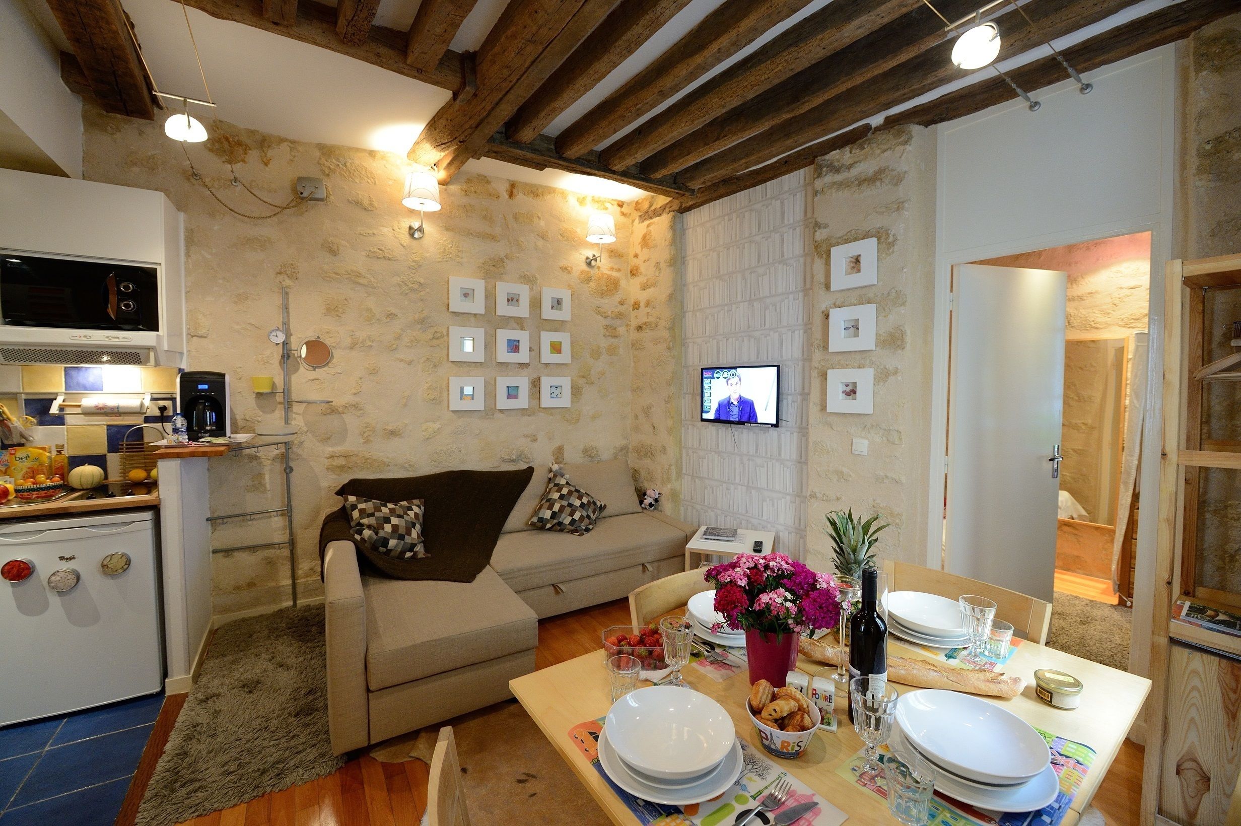 Un salon confortable avec une cuisine, une table à manger pour deux personnes et un téléviseur fixé au mur.