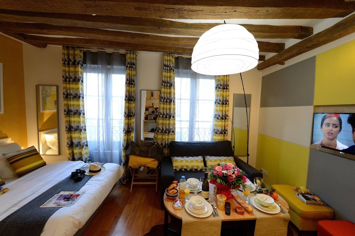 A hotel room with a bed, a sofa, a dining table set with breakfast, and a TV on the wall.