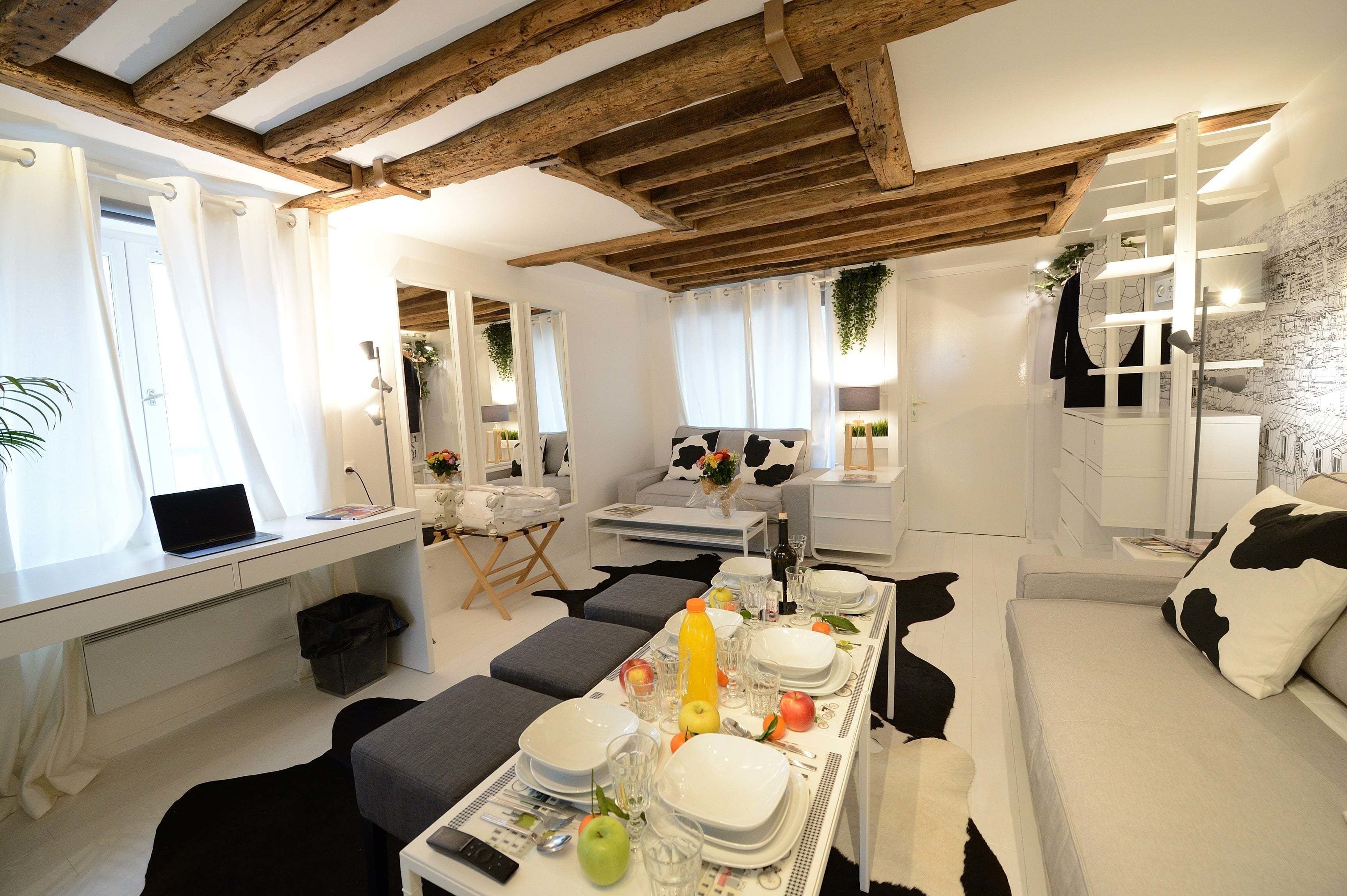 A modern, well-lit room with a dining table set for four, a sofa, and a desk with a laptop.