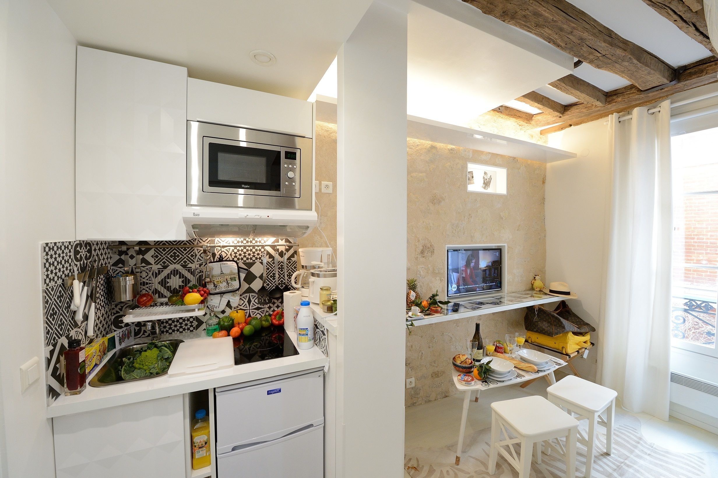 A compact kitchen with a microwave, sink, and a small refrigerator. There is a dining area with a table and two chairs.