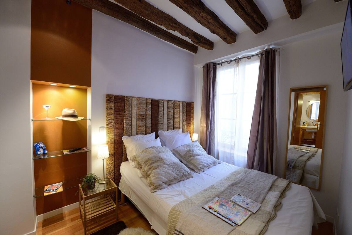 A neatly arranged bedroom with a wooden headboard, a bedside table with a lamp, and a mirror.
