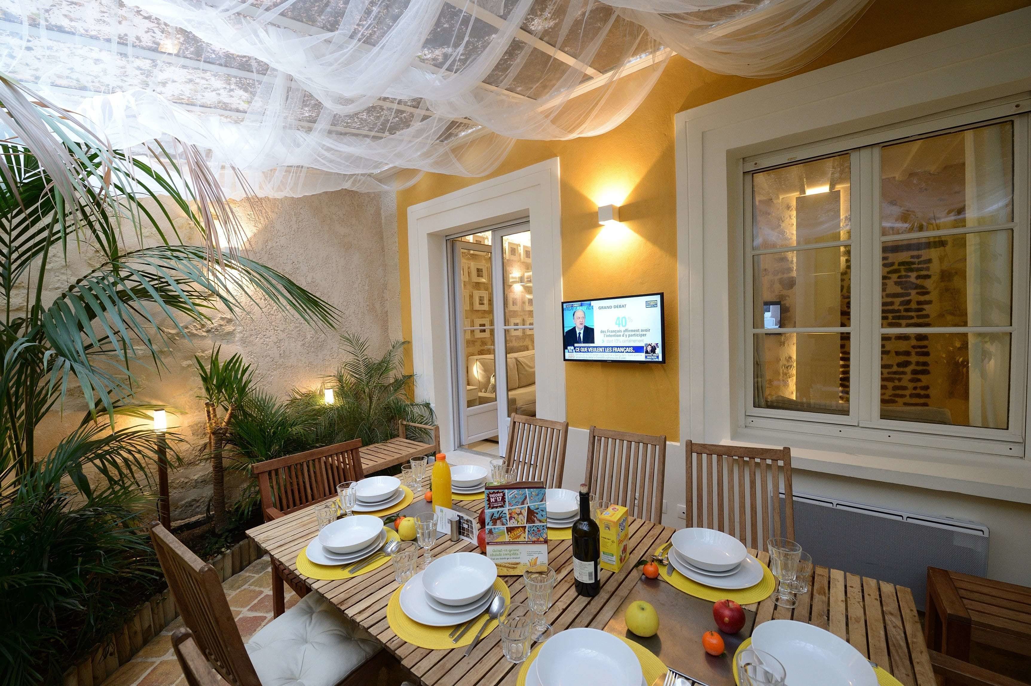 A dining area with a table set for four, surrounded by chairs, and a television mounted on the wall.