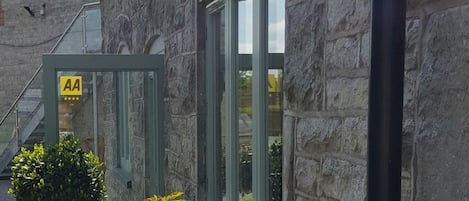 Un edificio de piedra con puerta de vidrio que indica 'AA' y un pequeño árbol en primer plano.