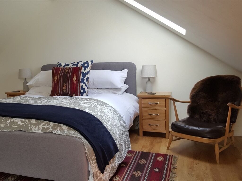 A bedroom with a bed, bedside tables, a chair, and a sloped ceiling.