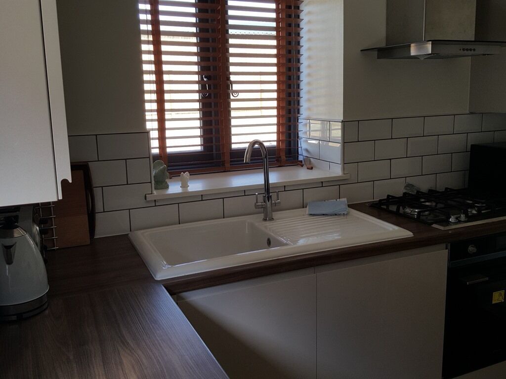 A kitchen with a white sink, wooden countertop, and a window with blinds.