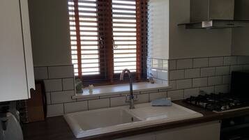 A kitchen with a white sink, wooden countertop, and a window with blinds.