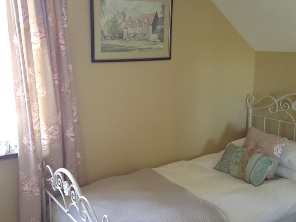 A bedroom with a bed, floral curtains, a framed picture on the wall, and a white metal headboard.