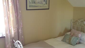 A bedroom with a bed, floral curtains, a framed picture on the wall, and a white metal headboard.