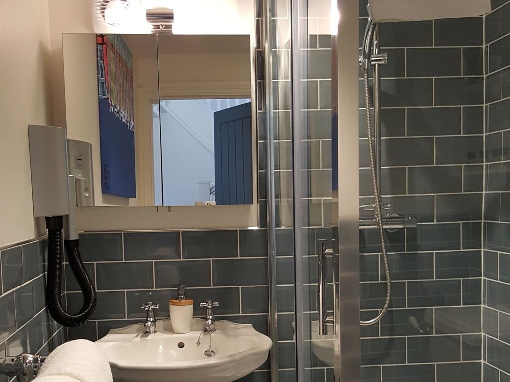 A bathroom with a glass shower enclosure, a sink with a mirror above it, and dark tiled walls.