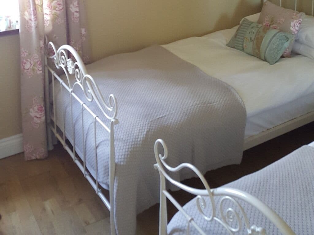 A single bed with a metal frame, a white mattress, and a floral-patterned curtain.