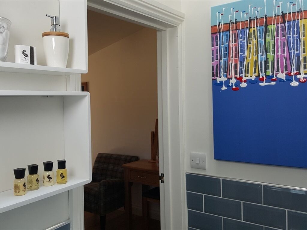 Een badkamer met een wit schap met toiletartikelen, een blauwe betegelde muur en een schilderij van zeilboten.