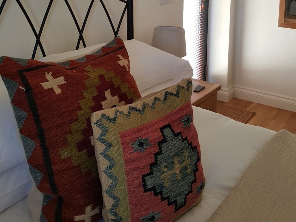 Una cama con dos almohadas estampadas y una colcha blanca.