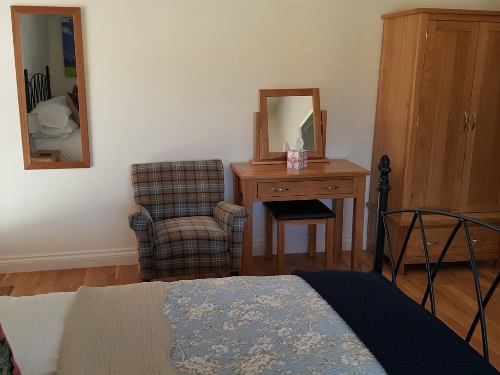 A bedroom with a bed, a chair, a wooden dresser, a mirror, and a wardrobe.