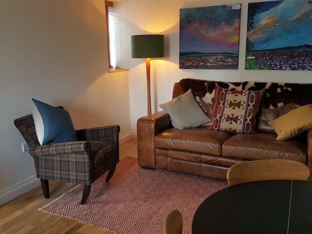 Una sala de estar con un sofá de cuero marrón, un sillón a cuadros y un tapete estampado.