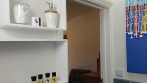 Une salle de bain avec des étagères blanches, des toilettes, un lavabo et un mur bleu orné d’un tableau coloré.