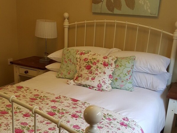 A bed with floral bedding, a white headboard, a bedside table with a lamp, and a wall painting. - The Natterjack Inn (Shepton Mallet)